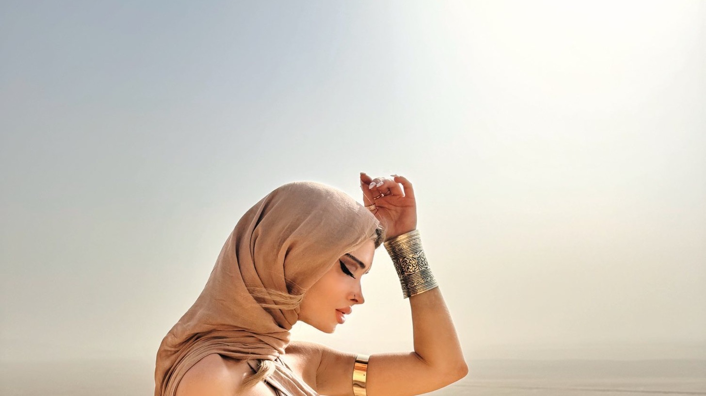 Dominique in a flowing sand-coloured veil and gold arm cuffs on a desert ridge